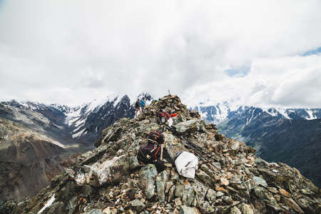 People on pinnacle of high mountain on background of glacier and snowy mountains. Guys conquered mountain peak. View to great mountain range among low clouds. Russia, Altai mountains, 14 July, 2019.のeditorial素材