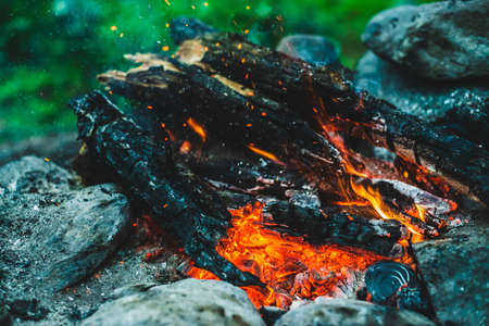 Vivid smoldered firewoods burned in fire close-up. Atmospheric background with orange flame of campfire. Full frame image of bonfire. Warm whirlwind of glowing embers and ashes in air. Sparks in bokehの写真素材