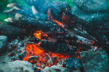 Vivid smoldered firewoods burned in fire closeup. Atmospheric background with orange flame of campfire. Full frame image of bonfire with sparks in bokeh. Warm vortex of glowing embers and ashes in airの写真素材