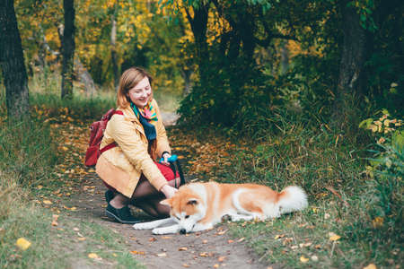 Young red husky dog playing with girl in park. Beautiful woman and foxy dog in autumn colors. Girl plays with white ginger husky in fresh air. Walking pet with owner in outdoors. Colorful autumn sceneの写真素材