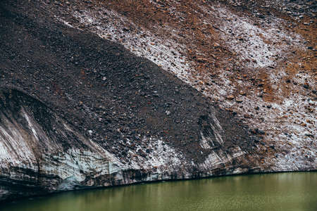Stones on slope of glacier above mountain lake of acid green color. Beautiful emerald glacial lake and snowy slope of glacier with stones. Awesome alpine lake of unusual green tones. Amazing landscapeの写真素材