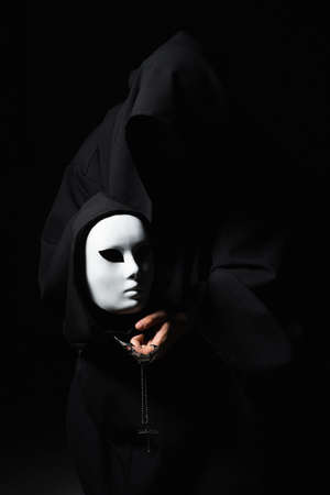 Vicious mage in black mantle and demon in sleeve. Ritual deal with devil. Man with split personality. Schizo talking to mask. Cursed assassin end evil spirit in dark room. Monk curse. Evil sorcerer.の写真素材