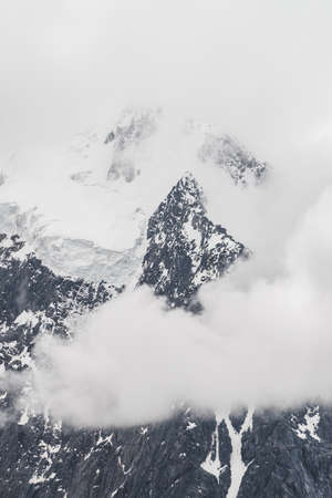 Atmospheric minimalist alpine landscape with massive hanging glacier on snowy mountain peak. Big balcony serac on glacial edge. Low clouds among snowbound mountains. Majestic scenery on high altitude.の写真素材