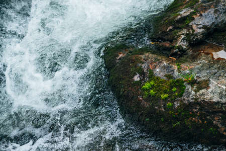 Big stones with moss and lichen in water riffle of mountain river. Powerful water stream of mountain creek. Natural textured rapid background of fast flow of mountain brook. Mossy boulders close-up.の写真素材