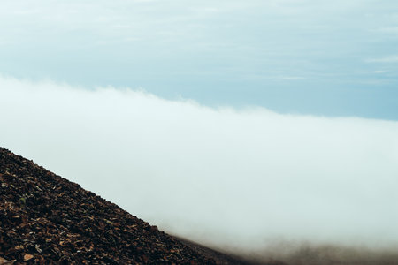 View from stony mountainside to highland valley within clouds. Atmospheric minimalist alpine landscape with low clouds in mountain valley. Wonderful mountain scenery with thick clouds on ground.の写真素材