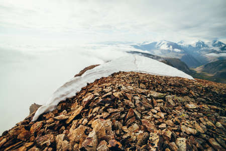 Footprints in snow on mountain top above thick clouds with view to giant mountains and glaciers....