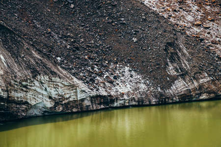 Stones on slope of glacier above mountain lake of acid green color. Beautiful emerald glacial lake and snowy slope of glacier with stones. Awesome alpine lake of unusual green tones. Amazing landscapeの写真素材