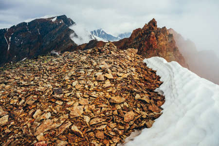 Beautiful pointy rocky pinnacle on mountain with snow among thick low clouds. Atmospheric minimalist alpine landscape. Sharp rocky mountain top above thick clouds in abyss. Wonderful highland scenery.の写真素材