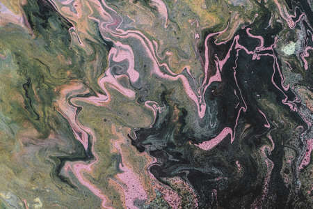 Dirty fluid art background with dark green, orange and pink tints and black stains. Eerie effect of...