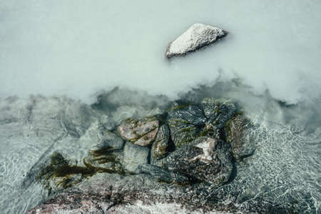 Nature background with mossy stones on silver water of mountain river. Silver sand on sandy bottom of mountain river. Shine on milky river surface. Gray nature backdrop with clear water with sand.の写真素材