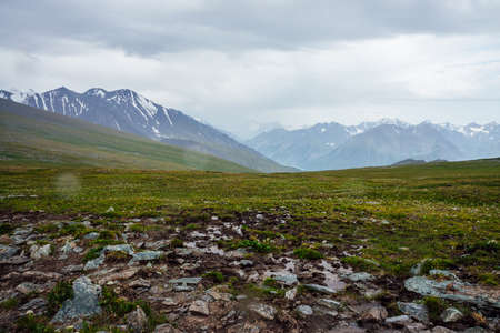 Beautiful view from pass to great snowy mountains under cloudy gray sky. Dramatic alpine landscape with snow mountains in rainy weather. Atmospheric scenery with giant mountain ridge in overcast day.の写真素材