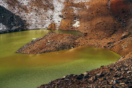 Stones on slope of glacier above mountain lake of acid green color. Beautiful emerald glacial lake and snowy slope of glacier with stones. Awesome alpine lake of unusual green tones. Amazing landscapeの写真素材