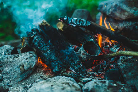 Vivid smoldered firewoods burned in fire close-up. Atmospheric warm background with orange flame of campfire and blue smoke. Unimaginable full frame image of bonfire. Burning logs in beautiful fire.の写真素材