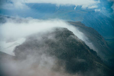 Atmospheric minimalist alpine landscape to giant low cloud among rocky mountain with snow. Low...
