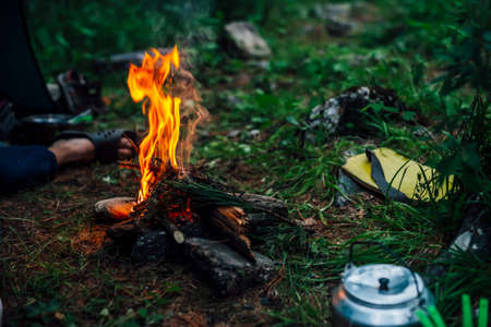 Camping kettle near small camp fire close-up. Cozy camping place in wild. Wonderful evening atmospheric background of campfire. Beautiful flame of small magic bonfire. Romantic warm place with fire.の写真素材