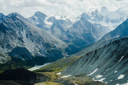 Footpath through hills to beautiful mountain valley with lake. Huge glacier mountains under gray...