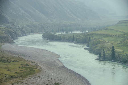 Beautiful misty mountain landscape with wide mountain river. Dark green gloomy scenery with big...
