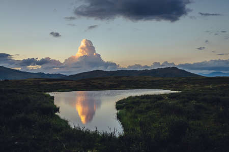Scenic sunset landscape with yellow big cloud in form of explosion above mountain lake. Awesome...