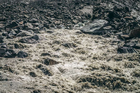 Scenic highlands landscape of powerful mountain river beginning from glacier among large moraines. Beautiful scenery with glacier at source of turbulent river. Mountain river source among big stones.の写真素材