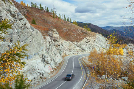 Car on mountain highway along rocks and trees with yellow foliage in sunshine in autumn. Colorful landscape with mountain road in fall time. Russia, Altai Republic, Chuysky tract, September 19, 2020.のeditorial素材