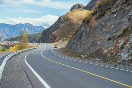 Car on mountain highway along rocks in sunshine in autumn colors. Colorful landscape with mountain road. Highway in mountains in fall time. Russia, Altai Republic, Chuysky tract, September 19, 2020.のeditorial素材
