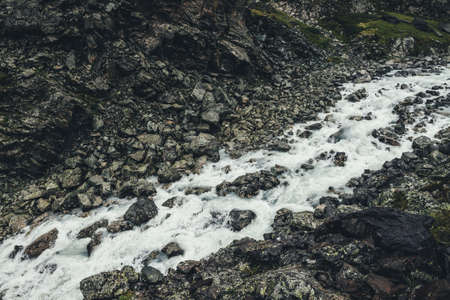 Atmospheric landscape with mountain creek among moraines in rainy weather. Bleak scenery with milky river among rocks. Gloomy view to mountain river. Stones with moss and lichen in milk water stream.の写真素材