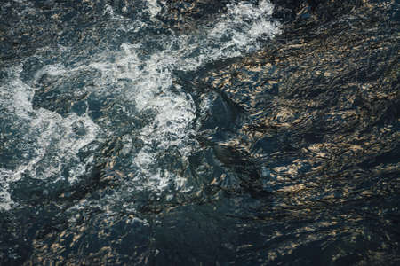 Atmospheric nature background of golden water of mountain river in sunrise or sunset. Scenic fragment of water surface with gold sunshine reflection. Sunlight reflected in golden blue water stream.の写真素材