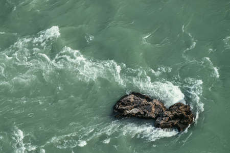 Minimal nature background of turquoise mountain river fragment. Big boulder in dark green mountain river flow closeup. Natural backdrop with big stone in water flow. Nature texture of water with rock.の写真素材