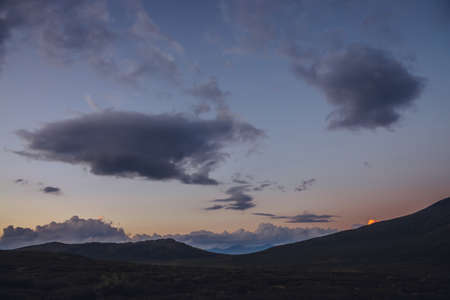 Atmospheric minimal mountain scenery with lilac dawn sky. Scenic minimalist landscape with purple sunset in mountains. Beautiful sunrise in mountains in pastel tones. Rocky mountain in dawn cloudy skyの写真素材