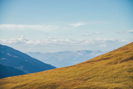 Minimalist autumn landscape with diagonal of sunlit orange mountainside on background of mountains silhouettes on horizon. Minimal mountain scenery with slope of hill in golden sunlight in autumn timeの写真素材