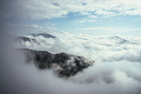 Wonderful alpine scenery with great rocks and mountains in dense low clouds. Atmospheric highlands landscape with mountain tops above clouds. Beautiful view to snow mountain peaks over thick clouds.の写真素材