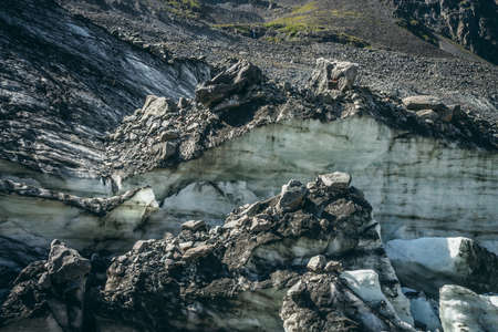 Nature background with icefall near glacier wall with cracks and scratches. Natural backdrop with icy wall and blocks of ice. Beautiful landscape with shiny glacial wall and ice blocks in sunlight.の写真素材