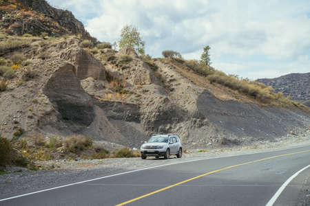 Car on mountain highway along rocks in sunshine in autumn colors. Colorful landscape with mountain road. Highway in mountains in fall time. Russia, Altai Republic, Chuysky tract, September 19, 2020.のeditorial素材