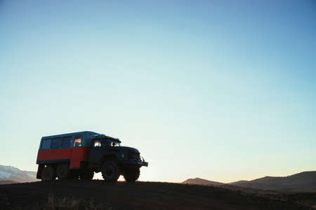 Truck on hill with view to great snow mountain range in sunlight. Sunset landscape with truck on background of snowy mountains in sunshine under blue sky. Russia, Altai Republic, 20 September, 2020.のeditorial素材