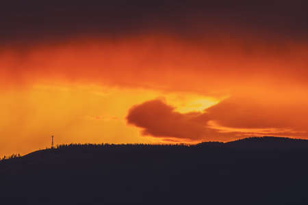 Atmospheric landscape with dark silhouette of mountain with trees on background of vivid orange dawn sky. Colorful nature scenery with sunset or sunrise of illuminating color. Vivid sundown paysage.の写真素材