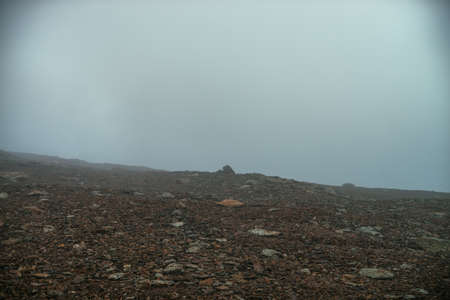 Stone field in dense fog in highlands. Empty stone desert in thick fog. Zero visibility in mountains. Minimalist nature background. Dark atmospheric foggy mountain landscape. Lichens on sharp stones.の写真素材