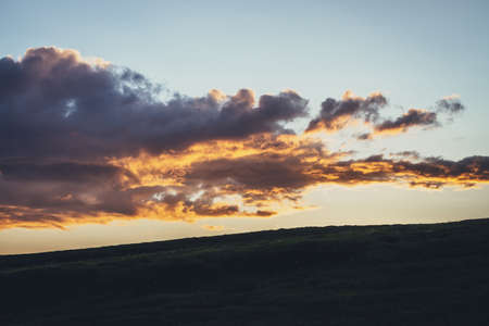 Beautiful mountain scenery with warm golden dawn light in cloudy sky. Scenic contrasting landscape with illuminating color in warm sunset sky. Gold illuminating sunlight. Contrast of warm sunrise sky.の写真素材