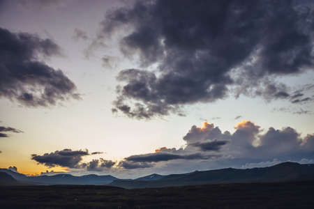 Beautiful mountain scenery with golden dawn light in cloudy sky. Scenic mountain landscape with illuminating color in sunset sky. Silhouettes of mountains on sunrise. Gold illuminating sunlight in skyの写真素材