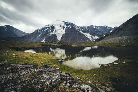 Scenic mountain landscape with glacial lake among mountains and glacier under gray cloudy sky. Atmospheric alpine scenery with transparent mountain lake in rainy weather. Beautiful clear alpine lake.の写真素材