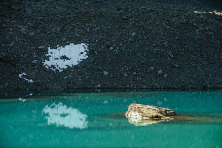 Beautiful scenic landscape with mossy rock in turquoise mountain lake. Azure glacial lake in sunlight. Colorful scenery with mossy stone above clear water surface. Sunny lake and stony mountain.の写真素材