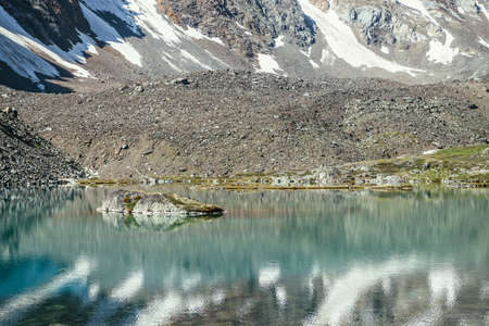Rock in turquoise mountain lake. Snowy mountain reflected in azure clear water of glacial lake. Beautiful sunny background with snow-white glacier reflection in green water surface of mountain lake.の写真素材
