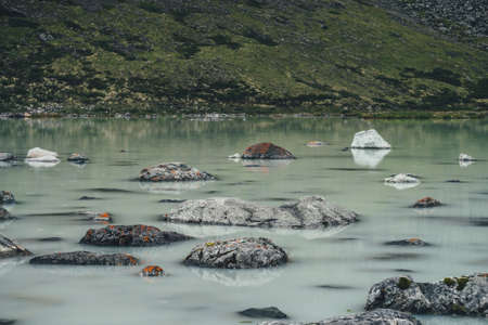 Scenic alpine landscape with rainy circles among stones with mosses and lichens in green water surface of swampy mountain lake. Atmospheric scenery with circles of rain in waterlogged mountain lake.の写真素材