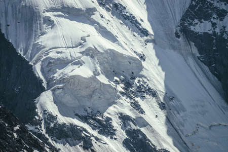 Nature background of big rocky snowy mountain wall with white glacier and snow cornice close up....