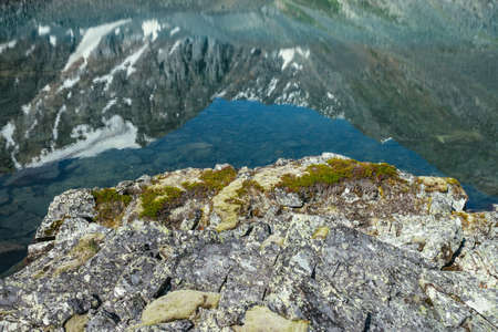 Snowy mountain reflected in clear water of glacial lake. Beautiful sunny landscape with snow-white glacier reflection in water surface of mountain lake. White snow on rock reflected in mountain lake.の写真素材