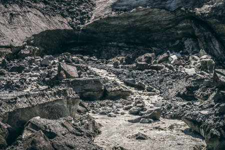 Scenic landscape with mountain river beginning from glacier among large moraines. Beautiful scenery with glacier at source of river. Mountain creek from ice among big stones. River source from glacierの写真素材