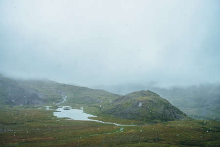 Beautiful snowfall with large snowflakes in high mountains. Mountain lake among hills during snowfall. Scenic landscape with flakes of snow. Atmospheric alpine scenery with snowfall in highlands.の写真素材