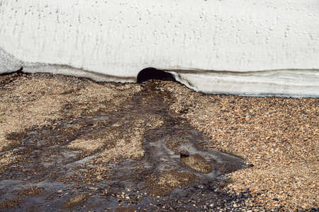 Scenic alpine landscape with small water stream among stones from small ice cave. Beautiful mountain scenery with streamlet from glacier. Closeup of ice wall with cave. Ice mountain wall close up.の写真素材