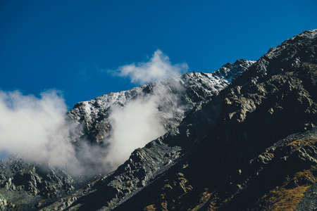 Atmospheric mountain landscape with high black rocky mountain with snow and low cloud on mountainside. Awesome alpine scenery with great dark mountain with low cirrus clouds. Snow and clouds on rocks.の写真素材