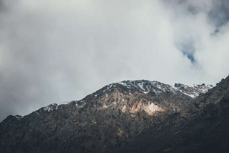 Mountain landscape with rocks with snow in sunlight and low clouds on top. Awesome rocky wall with...