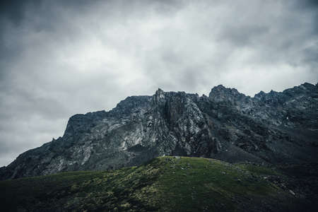 Dark atmospheric landscape with rocky mountain wall under gray cloudy sky. Rocky pinnacle in lead gray cloudy sky. Dark mountain peak in overcast weather. Gloomy minimalist scenery with high mountainsの写真素材